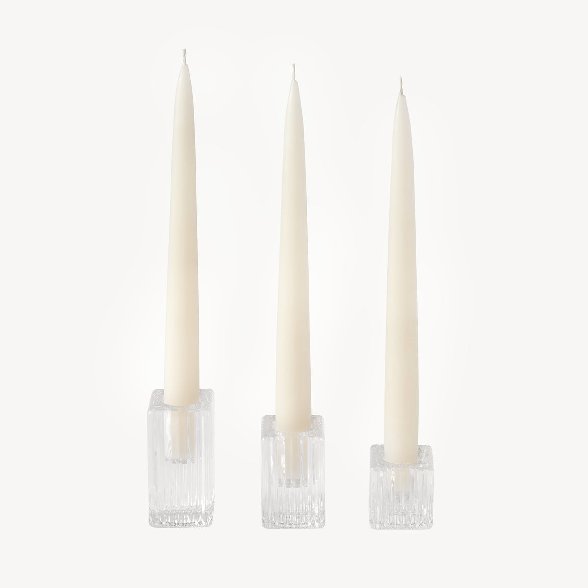 Three ivory taper candles in clear ribbed square glass candle holders of varying heights by Candle Flair
